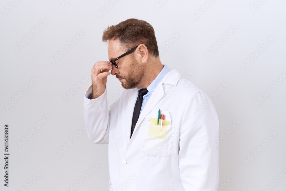 Middle age doctor man with beard wearing white coat tired rubbing nose and eyes feeling fatigue and headache. stress and frustration concept. Middle age doctor man with beard wearing white coat tired rubbing nose and eyes feeling fatigue and headache. stress and frustration concept.