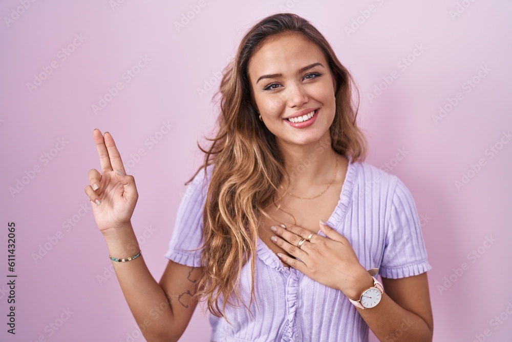 Young hispanic woman standing over pink background smiling swearing with hand on chest and fingers up, making a loyalty promise oath Young hispanic woman standing over pink background smiling swearing with hand on chest and fingers up, making a loyalty promise oath