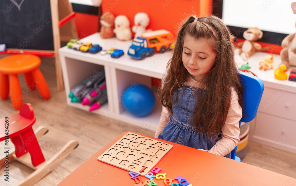 Fototapeta premium Adorable hispanic girl playing with maths puzzle game sitting on table at kindergarten