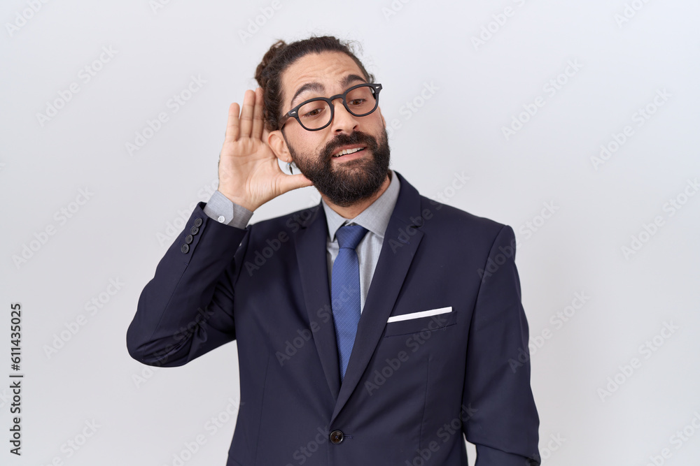 Hispanic man with beard wearing suit and tie smiling with hand over ear listening an hearing to rumor or gossip. deafness concept. Hispanic man with beard wearing suit and tie smiling with hand over ear listening an hearing to rumor or gossip. deafness concept.