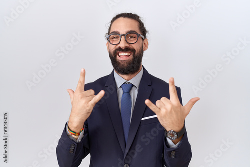 Hispanic man with beard wearing suit and tie shouting with crazy expression doing rock symbol with hands up. music star. heavy concept.