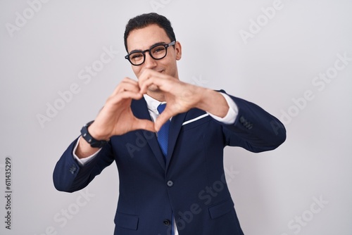 Young hispanic man wearing suit and tie smiling in love doing heart symbol shape with hands. romantic concept.