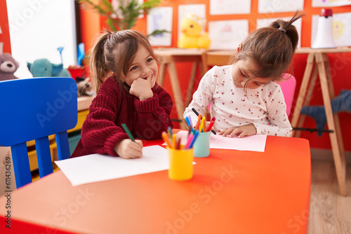 Adorable girls preschool students sitting on table drawing on paper at kindergarten