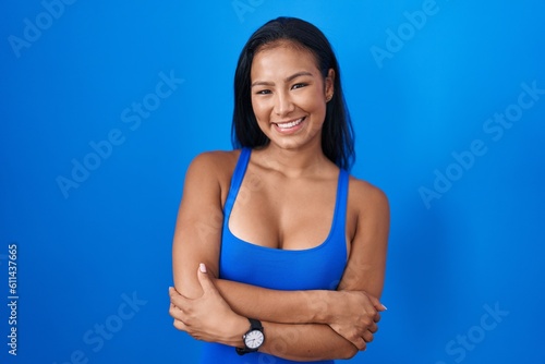 Hispanic woman standing over blue background happy face smiling with crossed arms looking at the camera. positive person.
