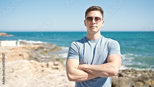 Young hispanic man tourist standing with crossed arms at seaside