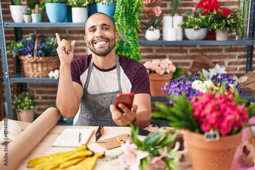 Hispanic man with beard working at florist shop with smartphone smiling happy pointing with hand and finger to the side