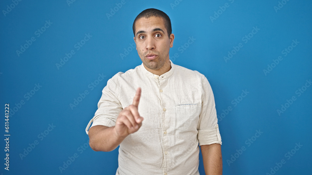 Young hispanic man saying no with finger over isolated blue background Young hispanic man saying no with finger over isolated blue background