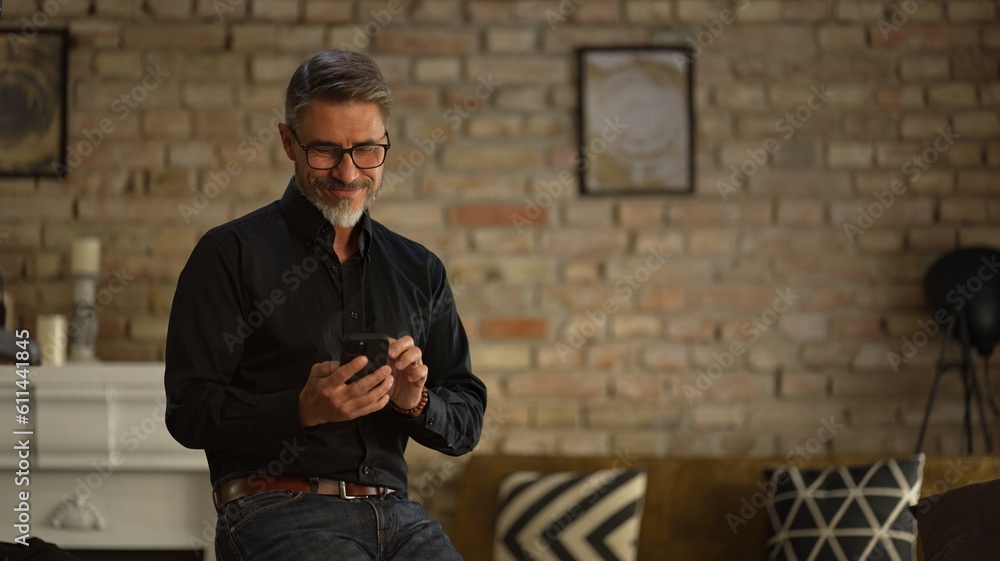 Portrait of happy, confident older man at home using phone, smiling. Mature age, middle age, mid adult casual guy in 50s, bearded, gray hair. Portrait of happy, confident older man at home using phone, smiling. Mature age, middle age, mid adult casual guy in 50s, bearded, gray hair.