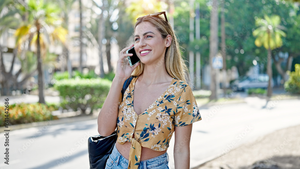 Young blonde woman smiling confident talking on smartphone at street