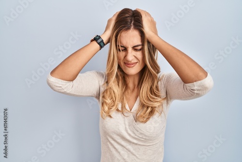 Young blonde woman standing over isolated background suffering from headache desperate and stressed because pain and migraine. hands on head.