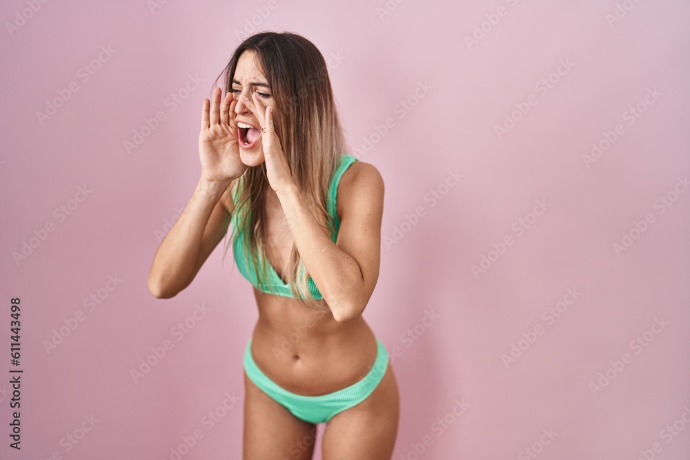 Naklejka premium Young hispanic woman wearing bikini over pink background shouting angry out loud with hands over mouth