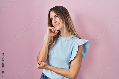 Young hispanic woman standing over pink background with hand on chin thinking about question, pensive expression. smiling with thoughtful face. doubt concept.