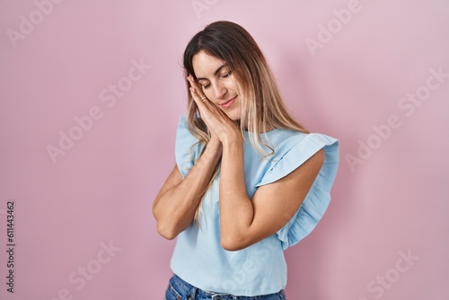 Young hispanic woman standing over pink background sleeping tired dreaming and posing with hands together while smiling with closed eyes.