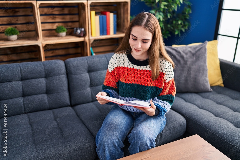 Young woman reading book sitting on sofa at home Young woman reading book sitting on sofa at home
