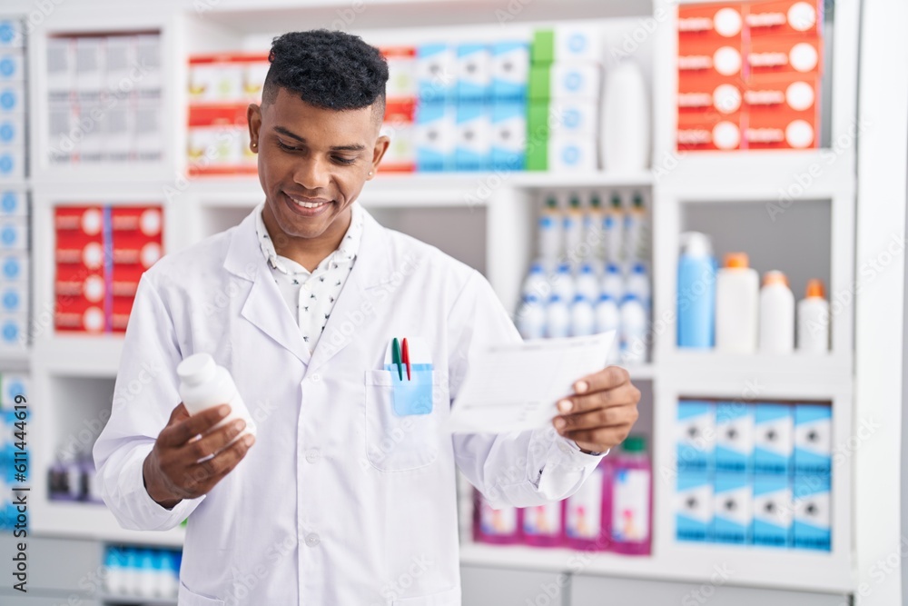 Young latin man pharmacist holding pills bottle reading prescription at pharmacy