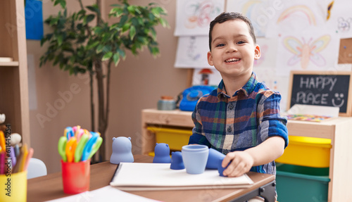 Adorable hispanic boy playing with toys sitting on table at kindergarten