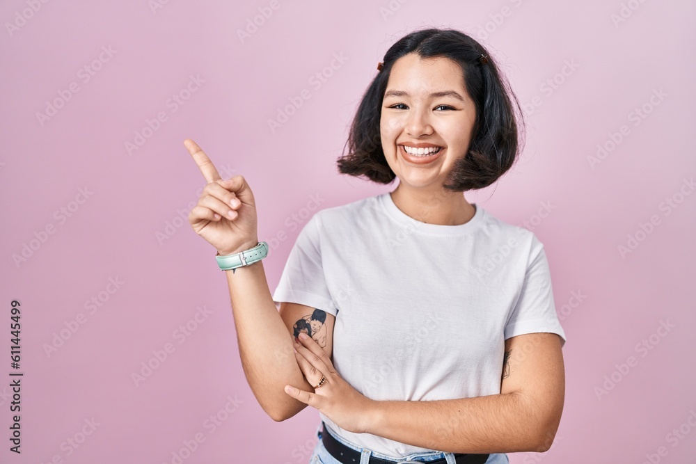 Young hispanic woman wearing casual white t shirt over pink background with a big smile on face, pointing with hand finger to the side looking at the camera. Young hispanic woman wearing casual white t shirt over pink background with a big smile on face, pointing with hand finger to the side looking at the camera.