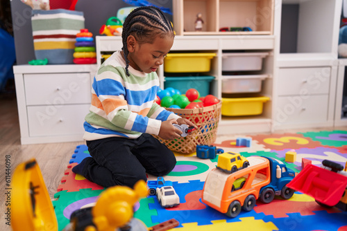 African american boy playing with car toy sitting on floor at kindergarten