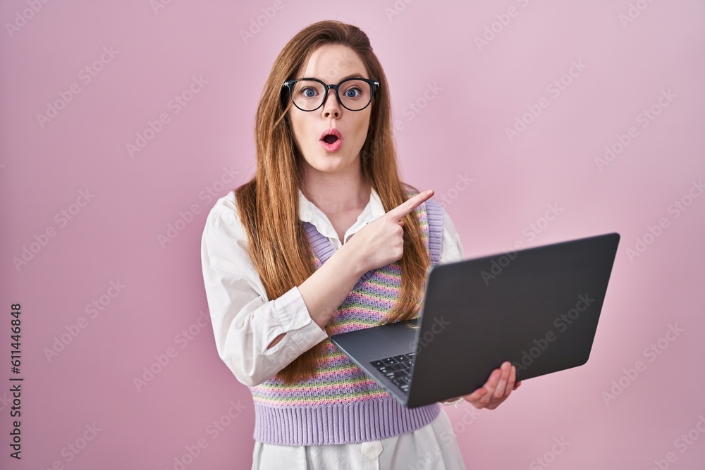 Young caucasian woman working using computer laptop surprised pointing with finger to the side, open mouth amazed expression. Young caucasian woman working using computer laptop surprised pointing with finger to the side, open mouth amazed expression.