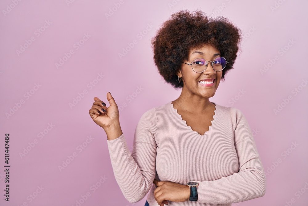 Young african american woman standing over pink background with a big smile on face, pointing with hand finger to the side looking at the camera. Young african american woman standing over pink background with a big smile on face, pointing with hand finger to the side looking at the camera.