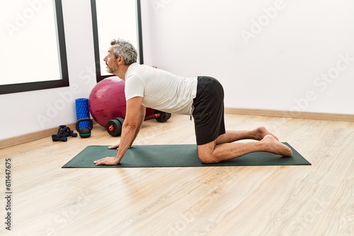 Middle age grey-haired man stretching back at sport center