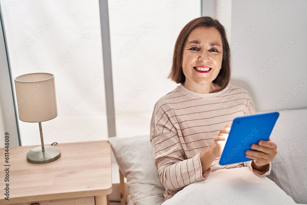 Middle age woman using touchpad sitting on bed at bedroom Middle age woman using touchpad sitting on bed at bedroom
