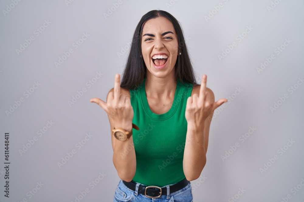 Young woman standing over isolated background showing middle finger doing fuck you bad expression, provocation and rude attitude. screaming excited Young woman standing over isolated background showing middle finger doing fuck you bad expression, provocation and rude attitude. screaming excited