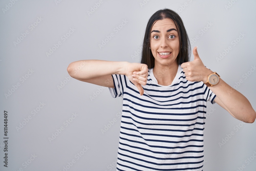 Young brunette woman wearing striped t shirt doing thumbs up and down, disagreement and agreement expression. crazy conflict Young brunette woman wearing striped t shirt doing thumbs up and down, disagreement and agreement expression. crazy conflict