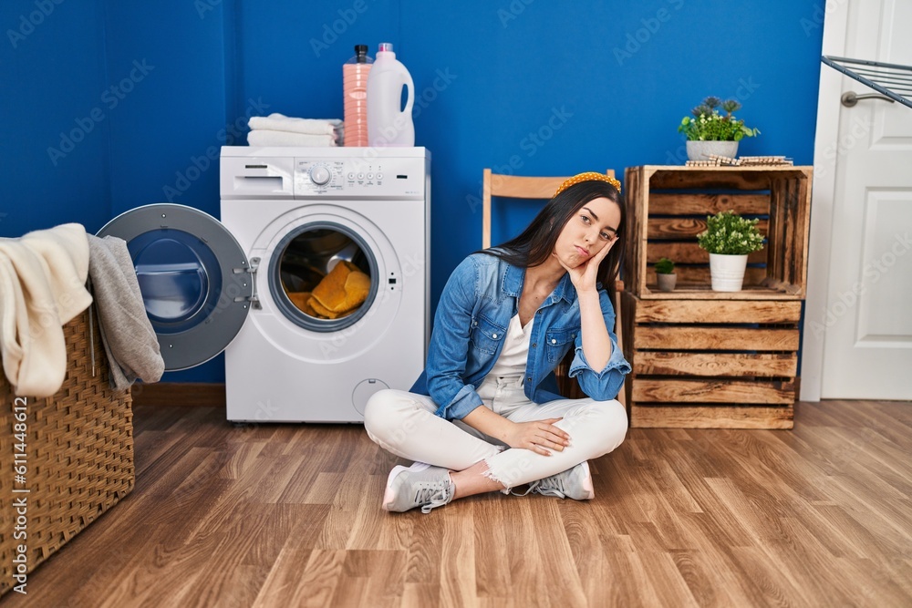 Hispanic woman doing laundry sitting on the floor thinking looking tired and bored with depression problems with crossed arms. Hispanic woman doing laundry sitting on the floor thinking looking tired and bored with depression problems with crossed arms.