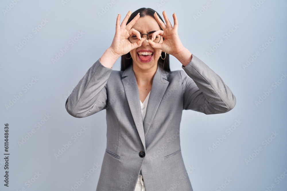 Hispanic business woman wearing glasses doing ok gesture like binoculars sticking tongue out, eyes looking through fingers. crazy expression. Hispanic business woman wearing glasses doing ok gesture like binoculars sticking tongue out, eyes looking through fingers. crazy expression.