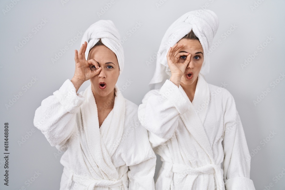 Middle age woman and daughter wearing white bathrobe and towel doing ok gesture shocked with surprised face, eye looking through fingers. unbelieving expression. Middle age woman and daughter wearing white bathrobe and towel doing ok gesture shocked with surprised face, eye looking through fingers. unbelieving expression.