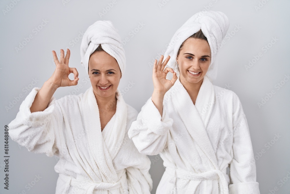Middle age woman and daughter wearing white bathrobe and towel smiling positive doing ok sign with hand and fingers. successful expression. Middle age woman and daughter wearing white bathrobe and towel smiling positive doing ok sign with hand and fingers. successful expression.