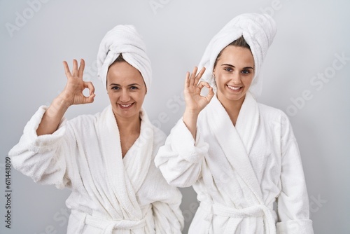 Middle age woman and daughter wearing white bathrobe and towel smiling positive doing ok sign with hand and fingers. successful expression.