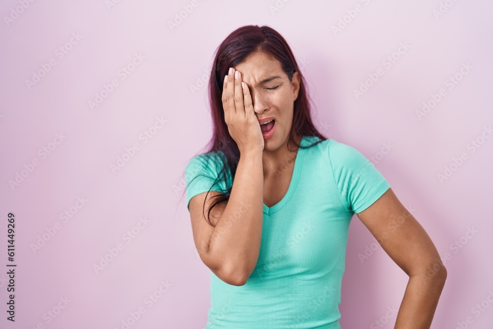 Young hispanic woman standing over pink background yawning tired covering half face, eye and mouth with hand. face hurts in pain. Young hispanic woman standing over pink background yawning tired covering half face, eye and mouth with hand. face hurts in pain.