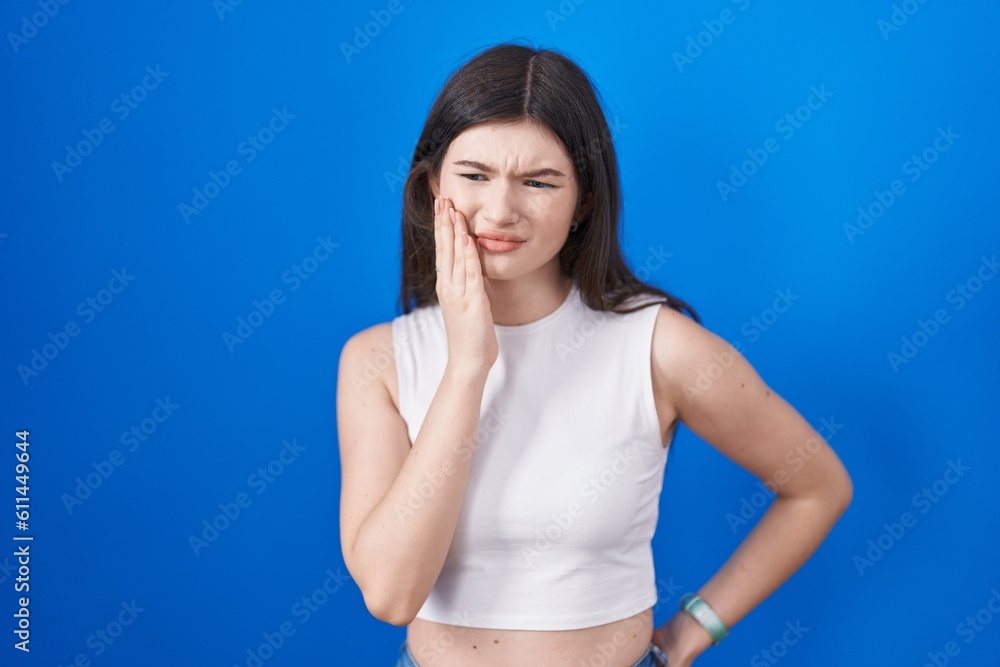 Young caucasian woman standing over blue background touching mouth with hand with painful expression because of toothache or dental illness on teeth. dentist Young caucasian woman standing over blue background touching mouth with hand with painful expression because of toothache or dental illness on teeth. dentist