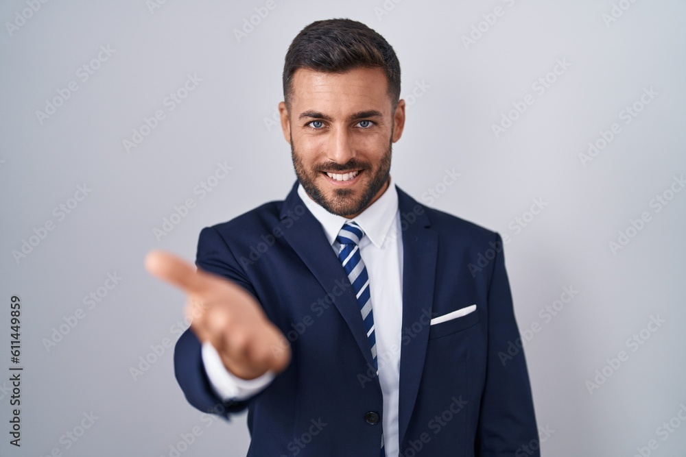 Handsome hispanic man wearing suit and tie smiling cheerful offering palm hand giving assistance and acceptance. Handsome hispanic man wearing suit and tie smiling cheerful offering palm hand giving assistance and acceptance.