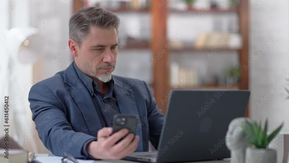 Businessman working with laptop computer and phone in home office. Portrait of happy confident middle aged, mid adult, mature age man smiling. Entrepreneur sitting at desk, managing business online. Businessman working with laptop computer and phone in home office. Portrait of happy confident middle aged, mid adult, mature age man smiling. Entrepreneur sitting at desk, managing business online.