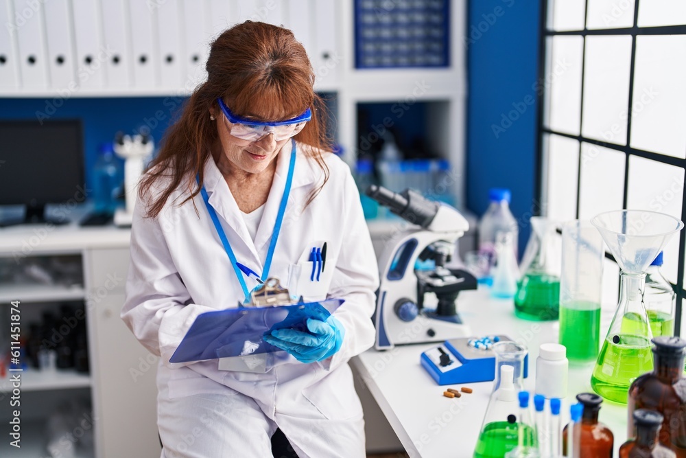 Middle age woman scientist smiling confident writing on clipboard at laboratory