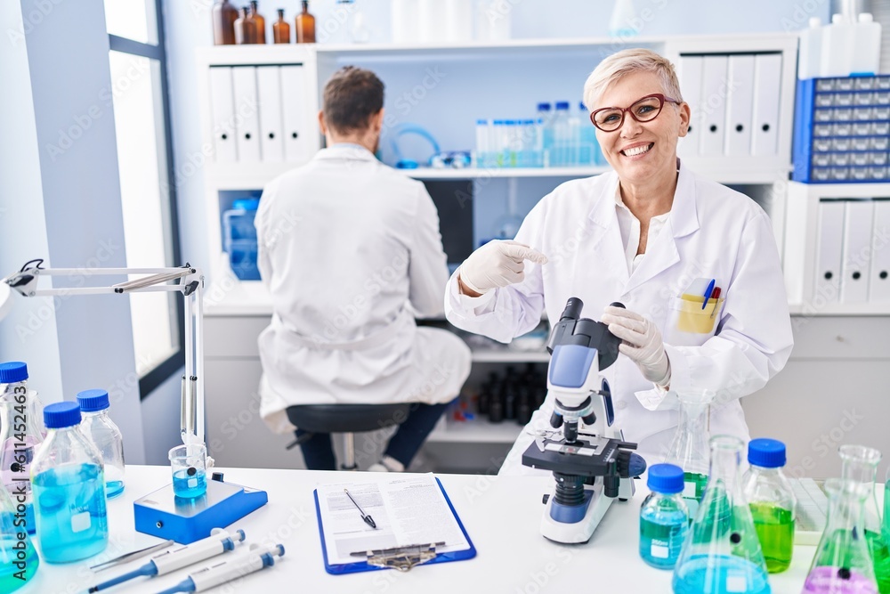 Middle age woman working at scientist laboratory smiling happy pointing with hand and finger Middle age woman working at scientist laboratory smiling happy pointing with hand and finger