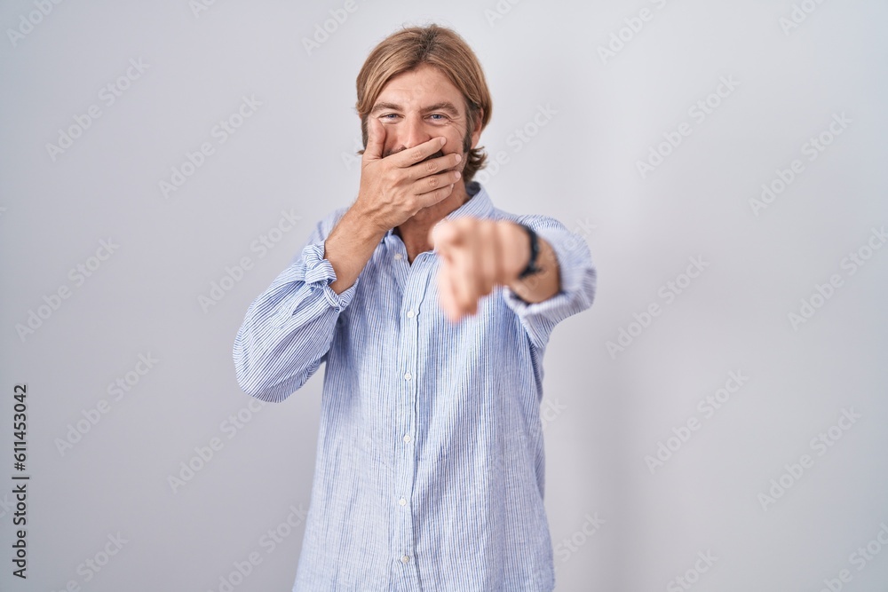 Caucasian man with mustache standing over white background laughing at you, pointing finger to the camera with hand over mouth, shame expression Caucasian man with mustache standing over white background laughing at you, pointing finger to the camera with hand over mouth, shame expression