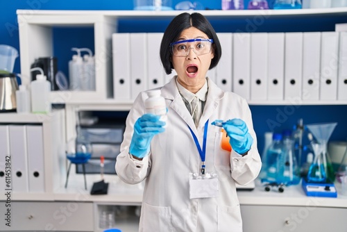 Young asian woman working at scientist laboratory afraid and shocked with surprise and amazed expression  fear and excited face.