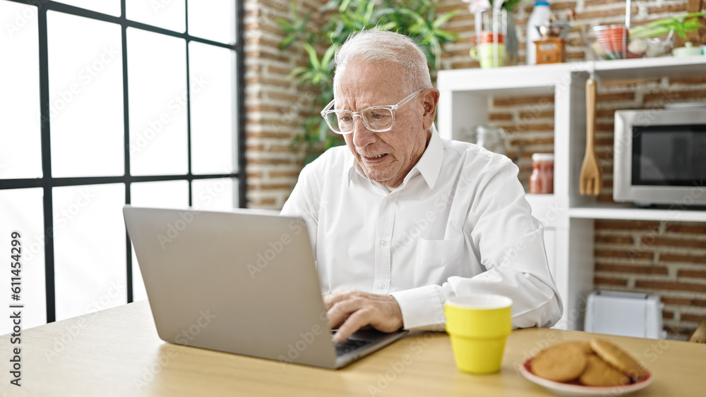 Senior grey-haired man using laptop wearing glasses at dinning room Senior grey-haired man using laptop wearing glasses at dinning room