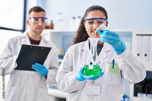 Man and woman wearing scientist uniform write on document measuring liquid at laboratory