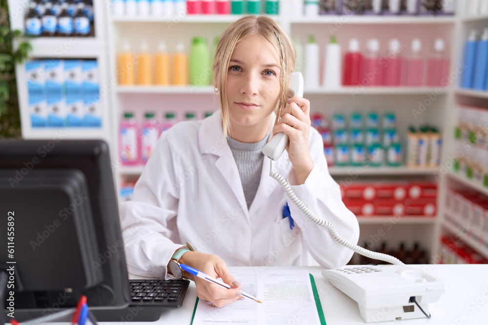 Young caucasian woman working at pharmacy drugstore speaking on the telephone relaxed with serious expression on face. simple and natural looking at the camera. Young caucasian woman working at pharmacy drugstore speaking on the telephone relaxed with serious expression on face. simple and natural looking at the camera.