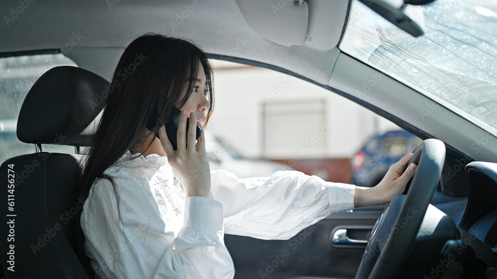 Young chinese woman talking on smartphone sitting on car at street