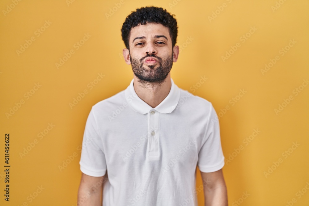Arab man standing over yellow background looking at the camera blowing a kiss on air being lovely and sexy. love expression. Arab man standing over yellow background looking at the camera blowing a kiss on air being lovely and sexy. love expression.