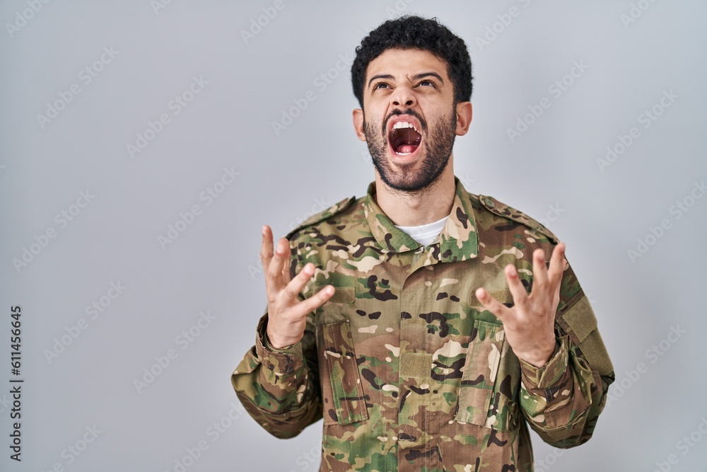 Arab man wearing camouflage army uniform crazy and mad shouting and yelling with aggressive expression and arms raised. frustration concept.