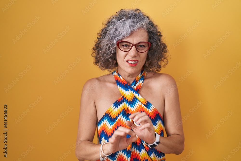 Obraz premium Middle age woman with grey hair standing over yellow background disgusted expression, displeased and fearful doing disgust face because aversion reaction.