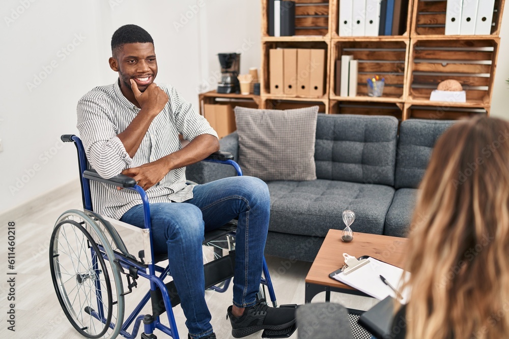 African american man doing therapy sitting on wheelchair looking confident at the camera smiling with crossed arms and hand raised on chin. thinking positive.