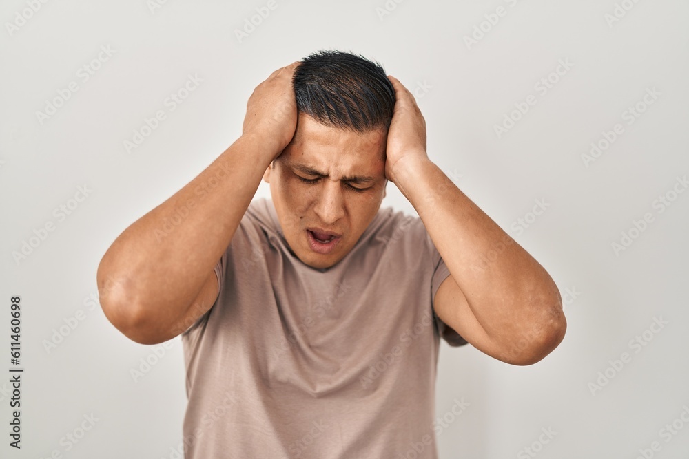 Hispanic young man standing over white background suffering from headache desperate and stressed because pain and migraine. hands on head. Hispanic young man standing over white background suffering from headache desperate and stressed because pain and migraine. hands on head.